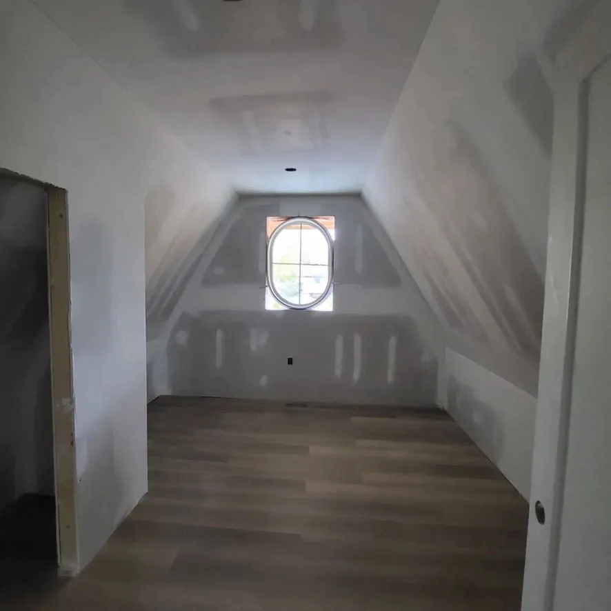 Taped sloped walls and ceiling around an oval dormer window.