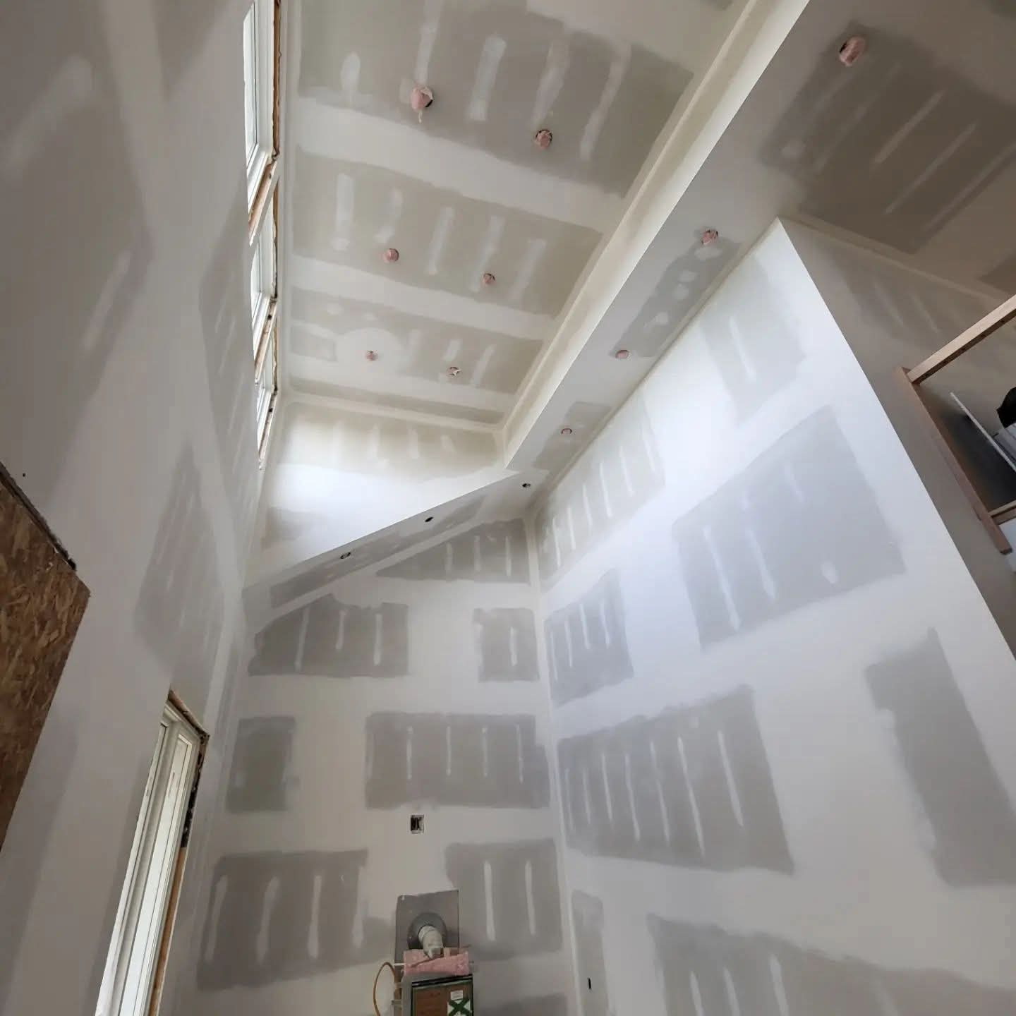 Double-height room with taped drywall across tall walls, ceiling transitions, and bulkheads