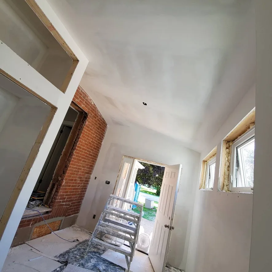 Drywall surfaces beside exposed brick and new window openings in an entry space.