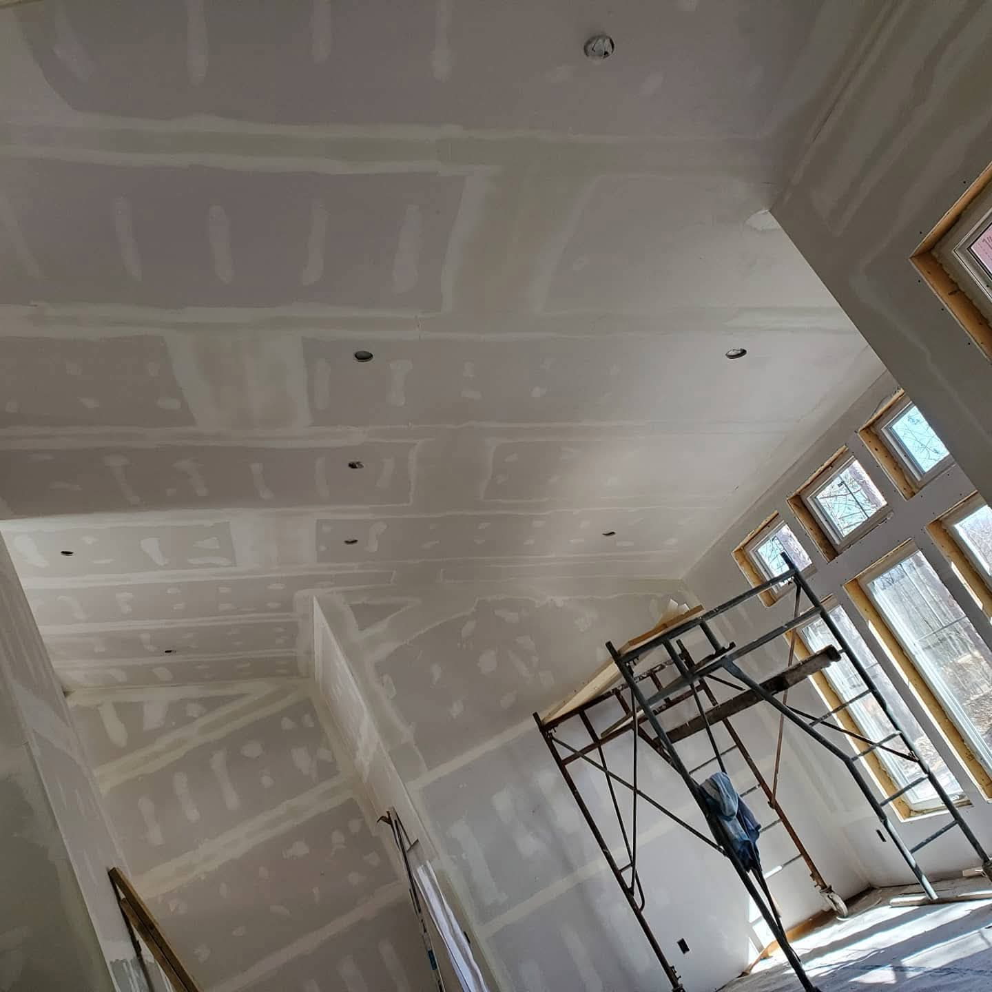 Large high-ceiling new-build interior with taped drywall, tall windows, and scaffold access