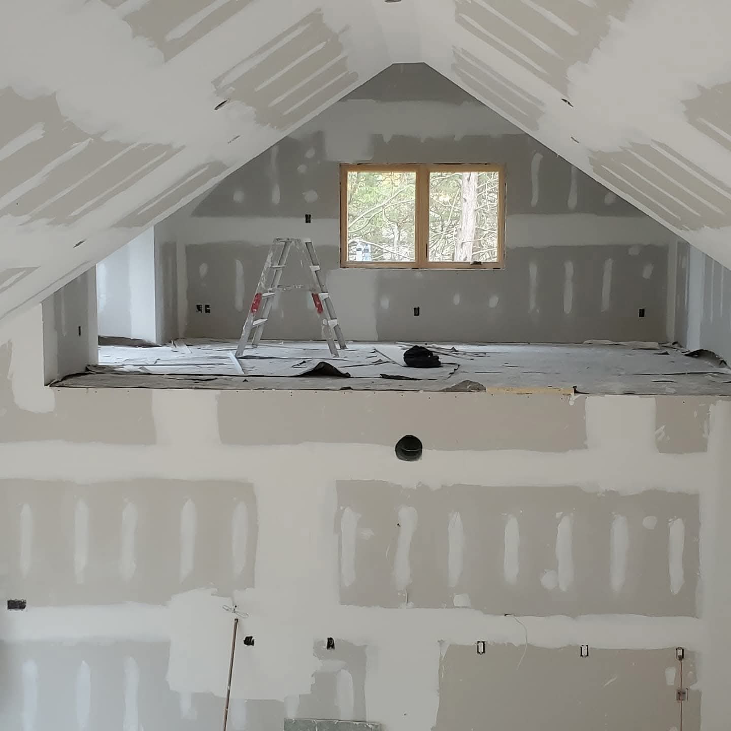 Open loft area with steep sloped ceilings and taped drywall across the full room