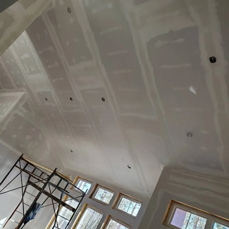 An upward view of long drywall seams across a tall vaulted ceiling.
