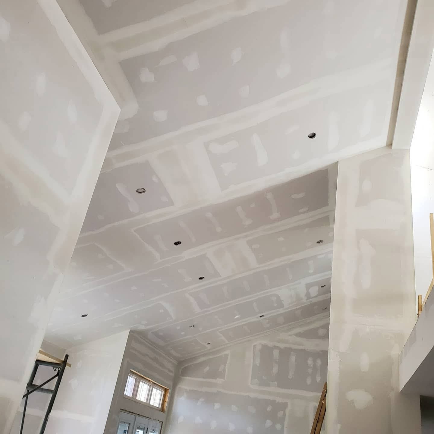 Vaulted great room with multiple ceiling planes, columns, and taped drywall throughout