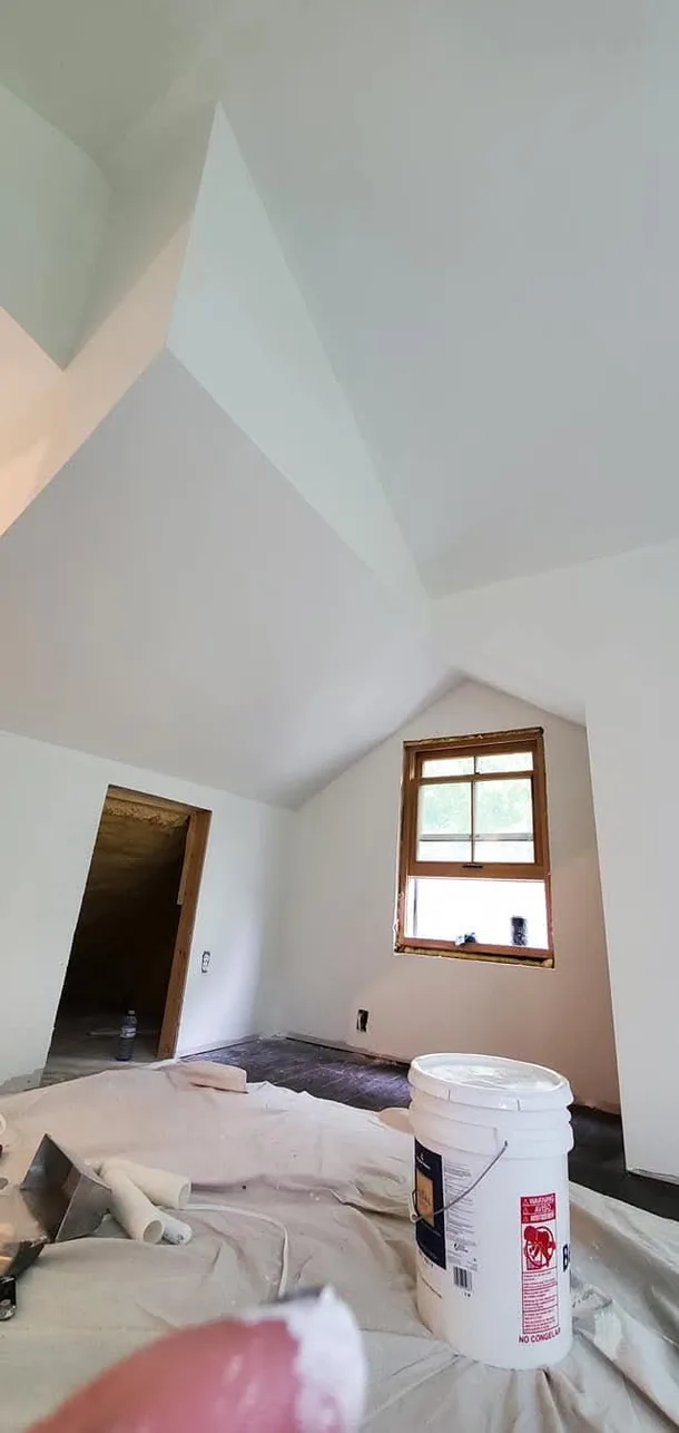 Smooth sloping ceiling surfaces and wall corners, with painting supplies still in place.